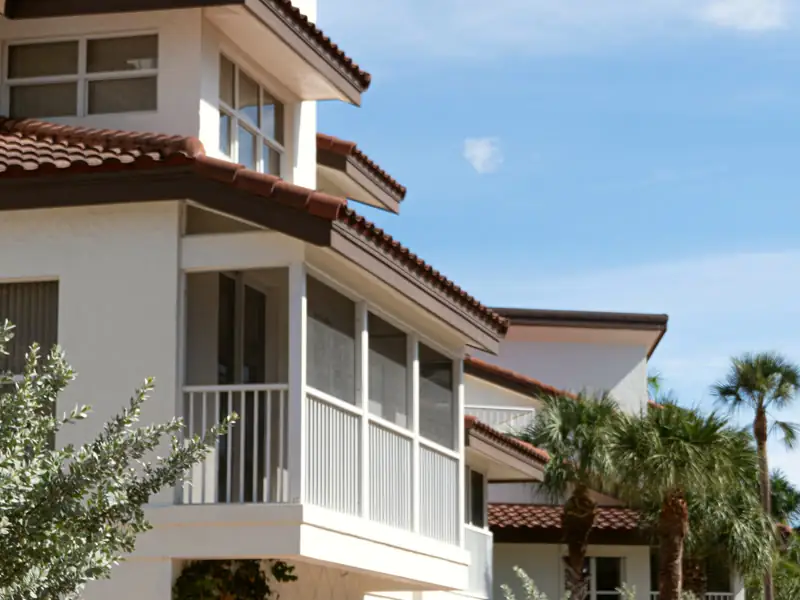 Bayshore Terrace Condo from the courtyard, a white building with a tile roof, arched garage doors and palms along a paver drive.