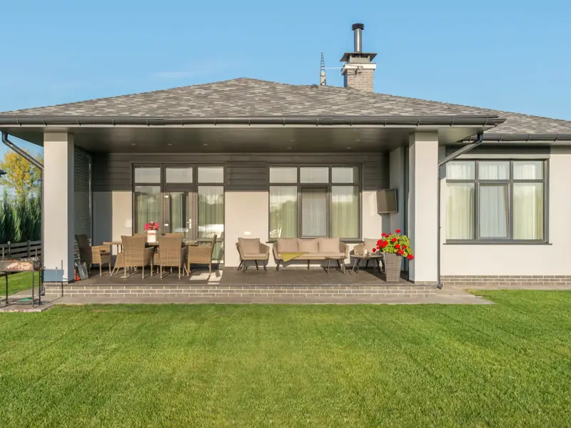 Lakewood Patio Home from the lawn, a single-story gray house with a hipped roof and a covered patio set with a dining table and sofa.