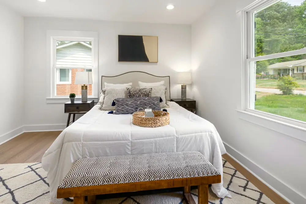The main-floor bedroom at Laurel Bend Ranch, a made bed with white linens, a bench at its foot and two bright windows.
