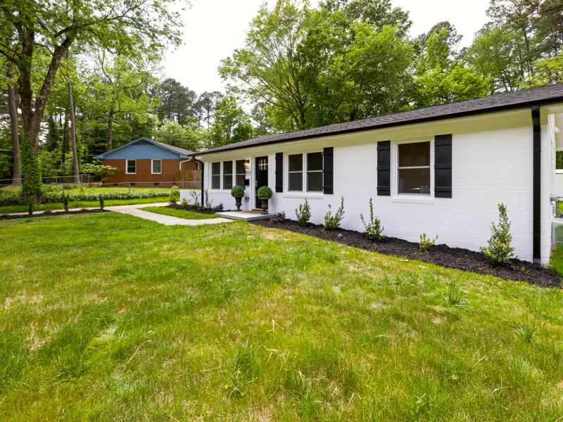 Laurel Bend Ranch from the lawn, a long white brick single-story house with black shutters and a level front walk.