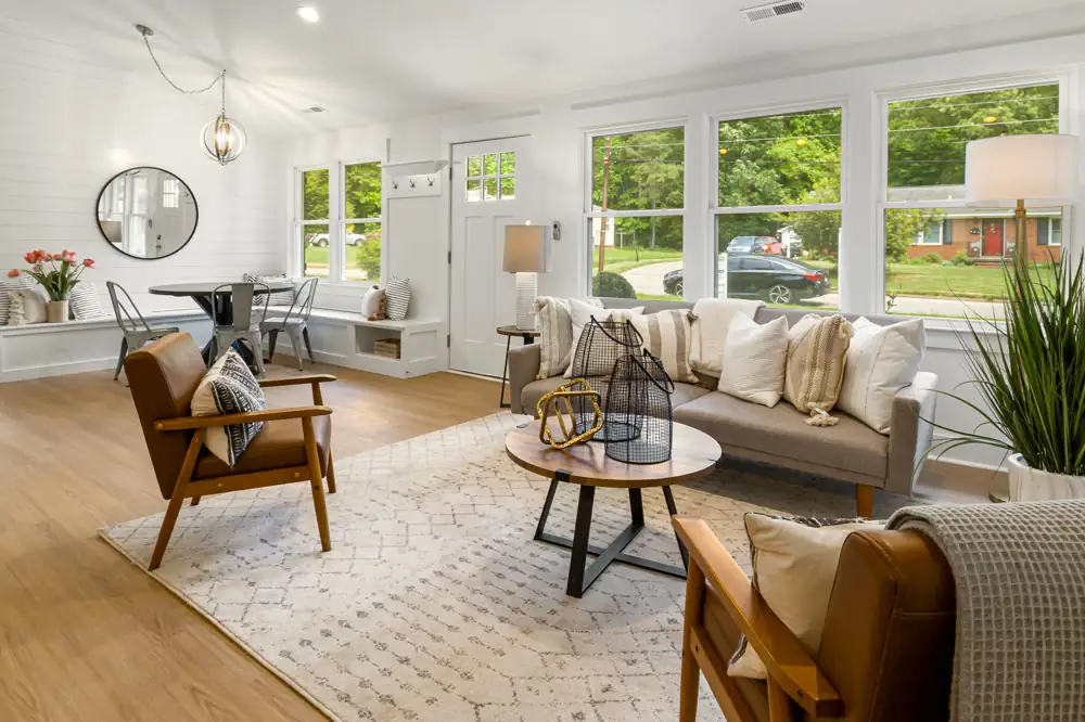 The living room at Laurel Bend Ranch, a gray sofa and two leather armchairs on light plank floors under a high ceiling, with a wall of windows.