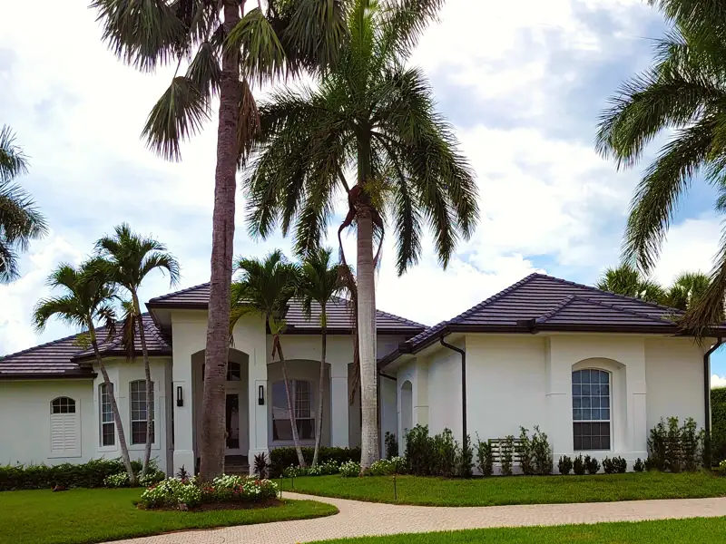 Palmetto Court Villa, a white stucco single-story home with a dark tile roof, tall palms and a curving paver walkway.
